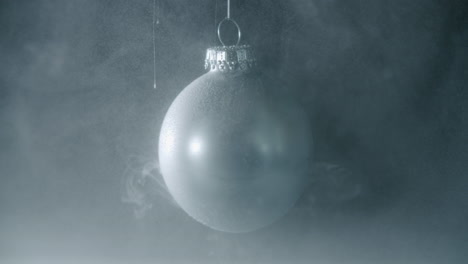 white dusty particles falling onto a a silver christmas bauble with black background