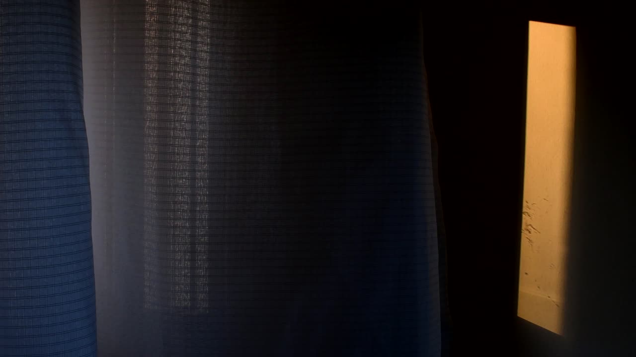 Et gardin bevæger sig langsomt i brisen, med varmt skumringslys, der falder på en nærliggende væg.