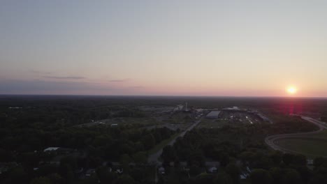 Las-Imágenes-De-Drones-Muestran-Un-Pequeño-Pueblo-De-Ohio-Rodeado-De-árboles-Mientras-El-Sol-Se-Pone-En-La-Distancia-Creando-Un-Tono-Naranja-En-El-Cielo-Despejado