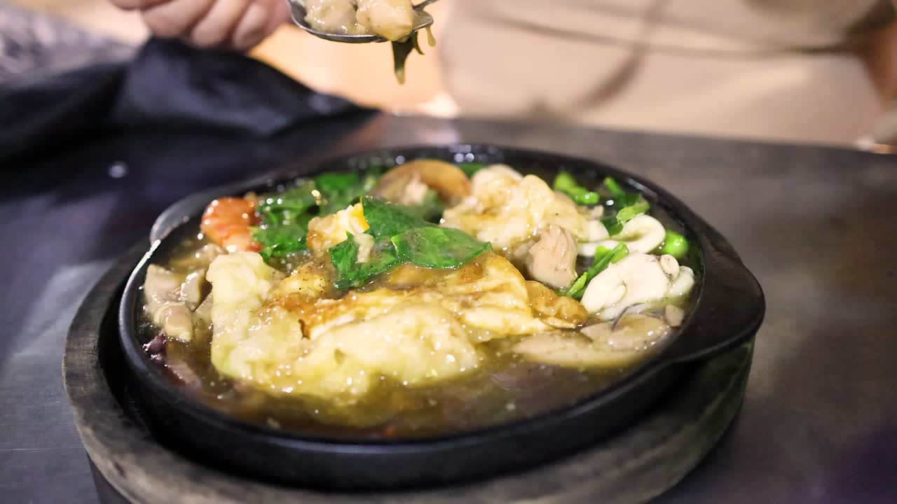 Person uses fork and spoon to eat steaming fried noodles at night street food market