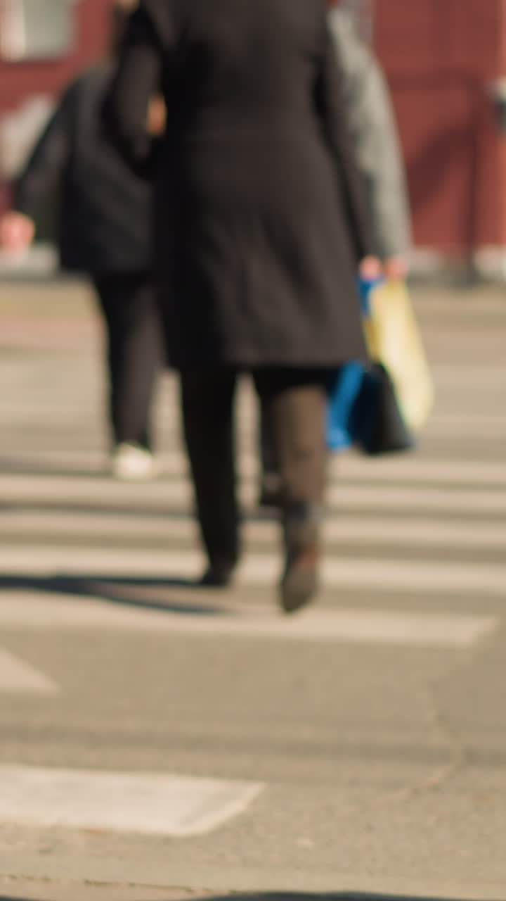 pedestrians crossing busy city crosswalk with shoppers and commuters, wide street view showing motion and blurred figures, yellow bag visible among walkers, striped pavement and soft afternoon light