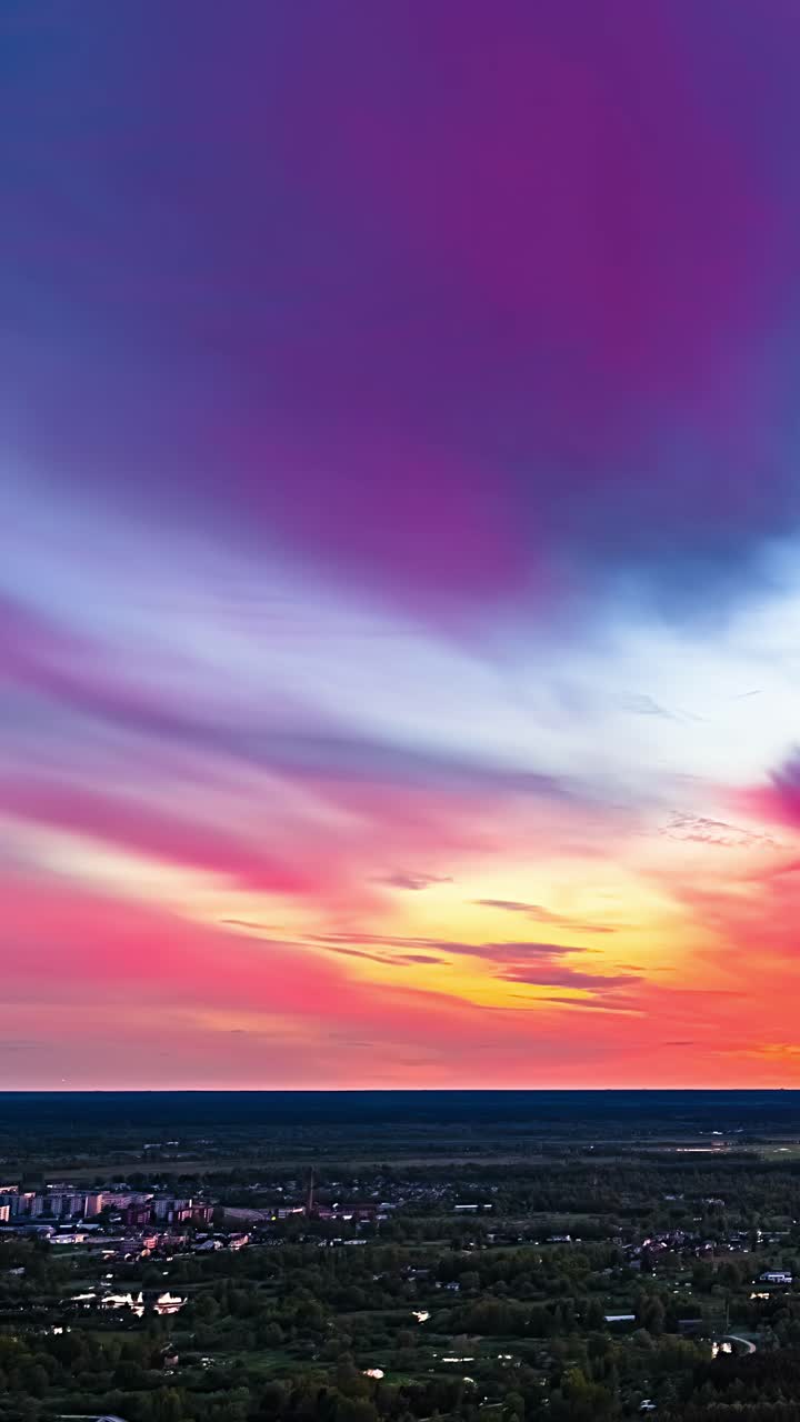 Dramatic sky fades from deep blue to rich red orange over forested town in timelapse