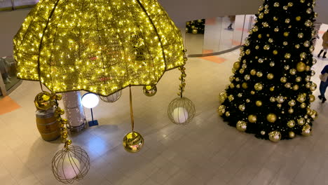 big christmas tree decorated with golden balls in a shopping mall, people walking on background wearing masks