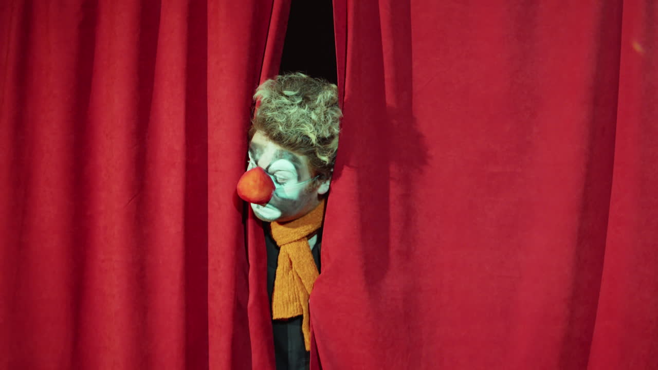 payaso mirando a través de las cortinas del escenario y realizando comedia