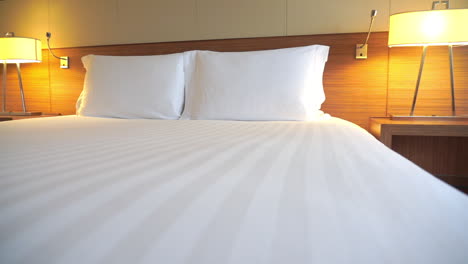 low angle panning shot of a white clean bed with two lamps on the sides in an empty hotel room