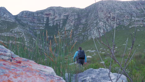 man hiking up trail towards big sandstone mountain, with drone backpack on back