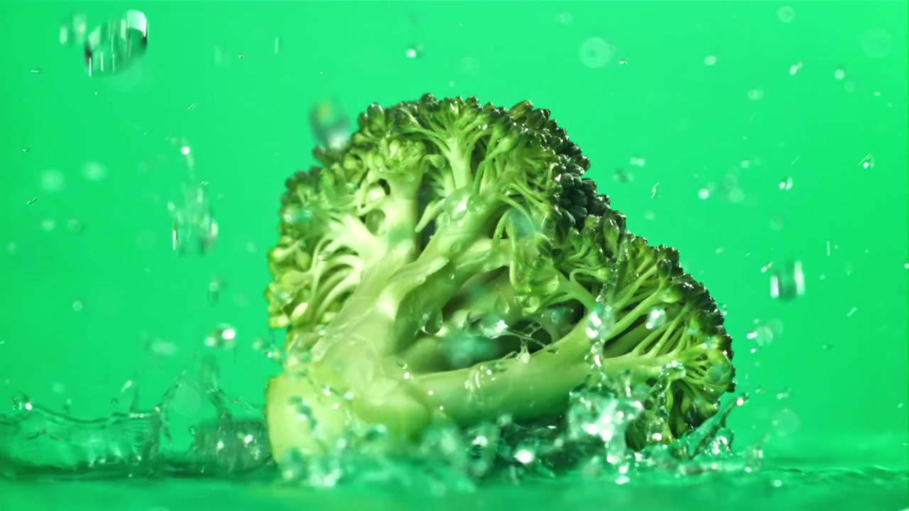 Cimetta di broccolo fresco con acqua che schizza su sfondo verde al rallentatore