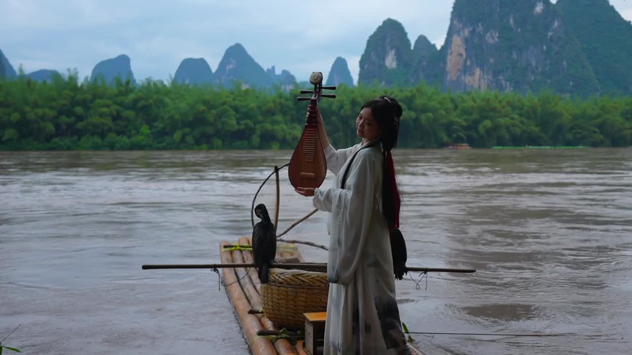 Hanfu girl poses with Pipa on bamboo raft with a mountainous background