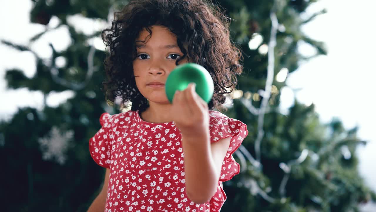 Menina decorando árvore de Natal com um enfeite verde