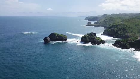 aerial view of rock island in ocean,hit by waves during sunny day - timang island, yogyakarta, indonesia