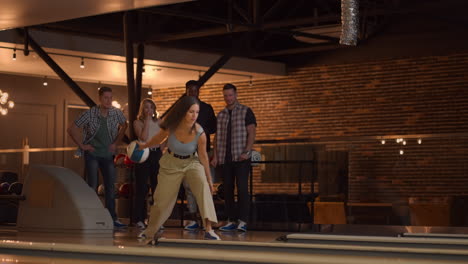 a caucasian brunette woman throws a bowling ball and knocks out a shot with one throw and hugs and rejoices with her friends. multi-ethnic group of friends bowling