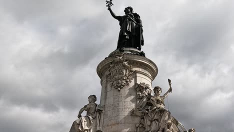 a towering statue on a pedestal with intricate sculptures, set against a dramatic cloudy sky.
