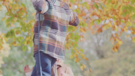 close up of brother and sister having fun on rope swing in autumn garden