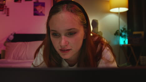 a young woman smiles as she uses her laptop in bed