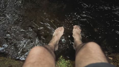 point of view of a man's feet sitting at the river with his feet in the water