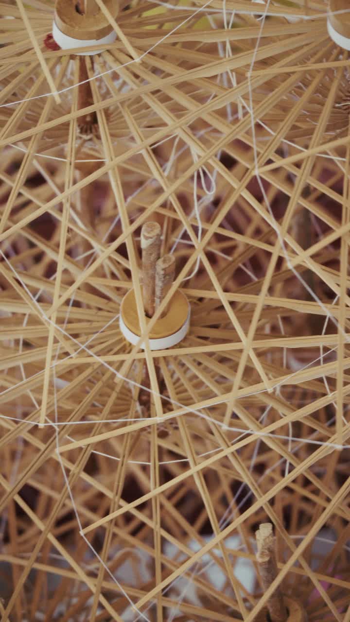 Zeitlupenaufnahme, die die innere Struktur eines handgefertigten Regenschirms enthüllt, der Bambusrippen, hölzerne Verbindungsstücke und sich kreuzende Fäden zeigt und dabei die traditionelle Handwerkskunst und die filigrane Konstruktion hervorhebt.