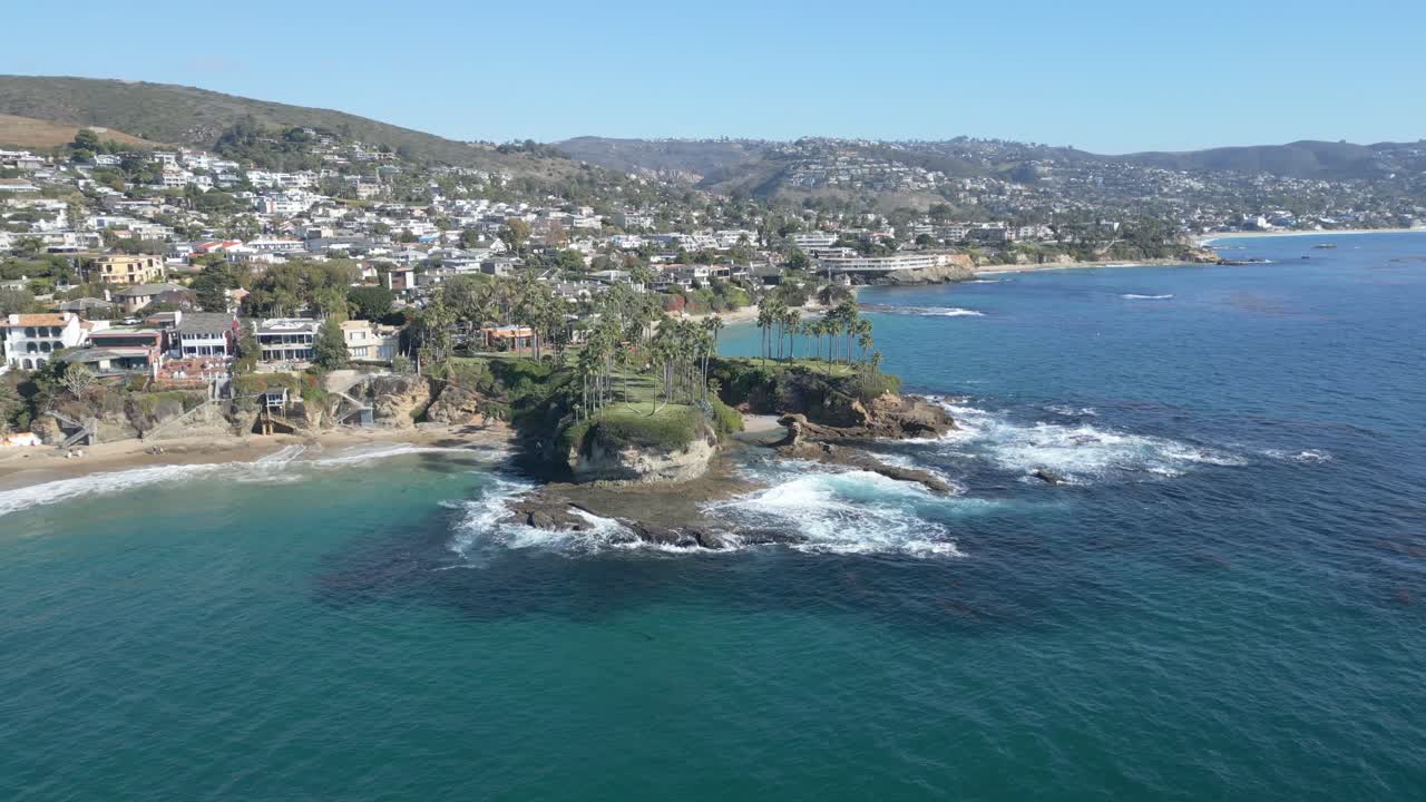 Calm 4K drone shot flying toward Laguna Beach shoreline, showcasing palm trees under bright sunny skies. Perfect for travel, tourism, or relaxing cinematic projects