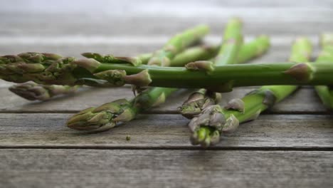 Slow-motion-footage-of-a-bunch-of-fresh,-green-asparagus-falling-on-to-a-wood-table