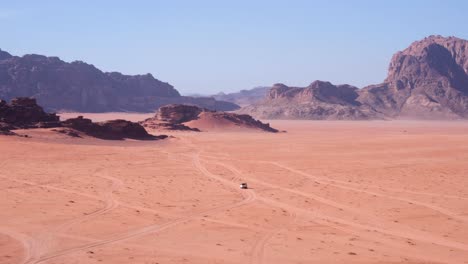 white 4wd truck driving across wadi rum desert in jordan, near the border of saudi arabia, remote, vast red sandy landscape