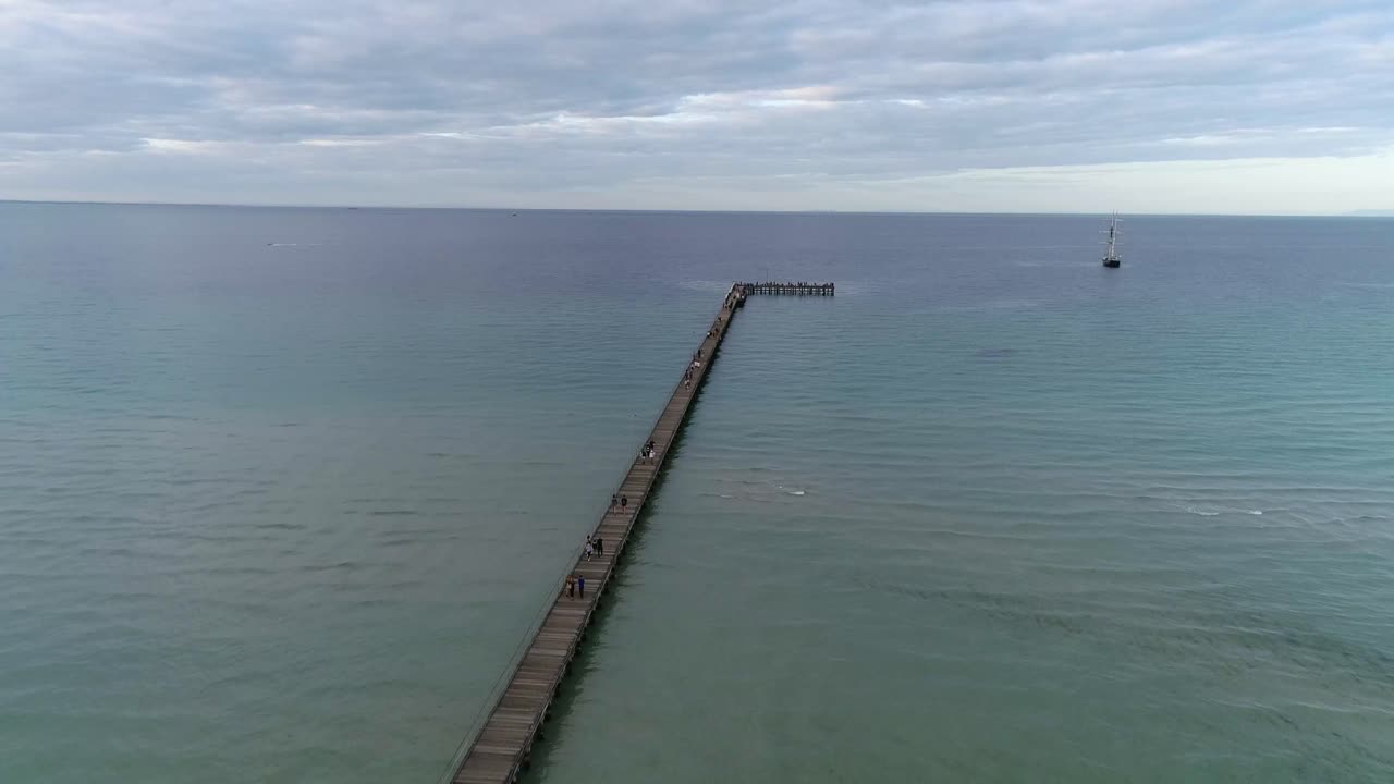 drone con vistas al largo muelle y al océano azul con el viejo velero centeno