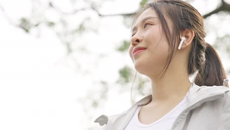4k 아시아 여성이 아침에 공원에서 조하는 동안 음악을 듣고 있습니다.