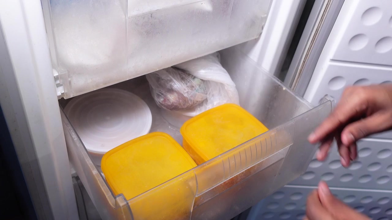 Persona che Inserisce un Contenitore Giallo per Alimenti nel Cassetto del Congelatore