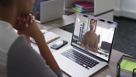 Afroamerikanische-Geschäftsfrau,-Die-Mit-Einem-Laptop-Am-Schreibtisch-Sitzt-Und-Einen-Videoanruf-Mit-Einem-Männlichen-Kollegen-Führt