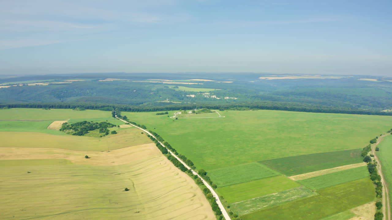 Drone shot of a picturesque landscape showing a village surrounded by farmlands, oak forest, and the historical archaeological reserve of "Sboryanovo", the Sveshtar Tomb in Bulgaria.