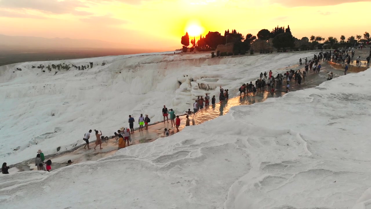 Turister går på hvide travertinterrasser i Pamukkale ved solnedgang