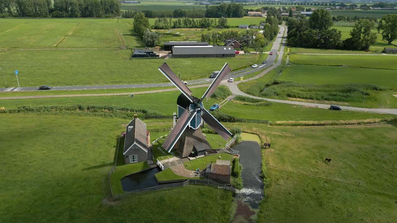 Slow drone approach of a classic Dutch windmill in lush countryside with narrow waterways and green fields