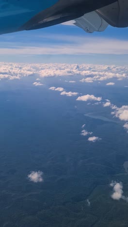 vertical view of landscape of belize from airplane window under wing, clouds and misty horizon