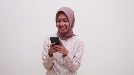 Cheerful-young-asian-muslim-woman-standing-while-using-cell-phone