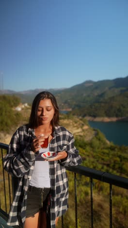 woman enjoying turkish tea on a balcony with a view of mountains and a river