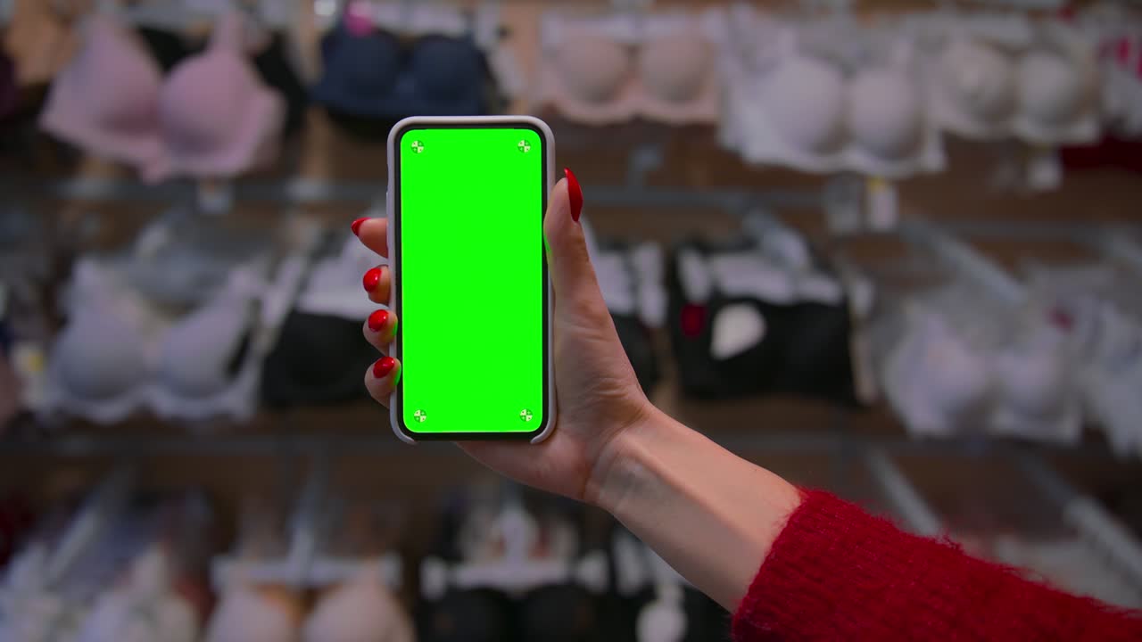 POV, female hand holding smartphone with blank green screen chromakey chooses underwear