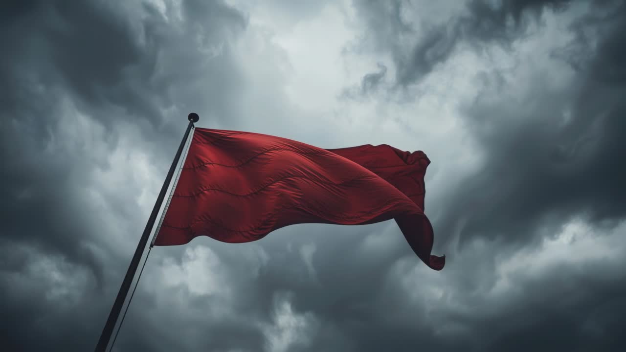 Czerwona flaga powiewająca na metalowym maszcie, reagująca na podmuchy wiatru, falująca na tle burzowego, zachmurzonego nieba