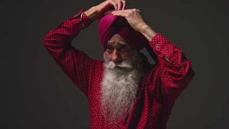 fotografía de iluminación de estudio de baja clave de un hombre sikh anciano con barba atando tela para turbante contra un fondo oscuro 13