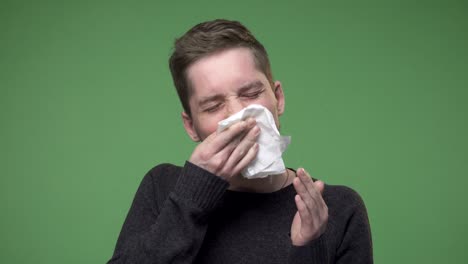 young man has cough a cold, he is using a handkerchief for his runny nose, chroma key green screen background