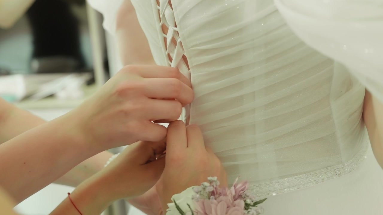 Tying the bride's dress. A close-up view of the hands lacing the back of the dress
