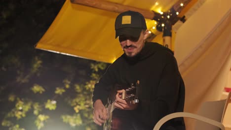 man plays the guitar and sings songs in a tent with light bulbs