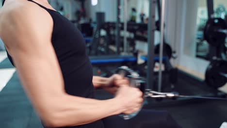 a woman in a black top performs an exercise for pumping the press and biceps against the background of sports equipment in a fitness club. close-up
