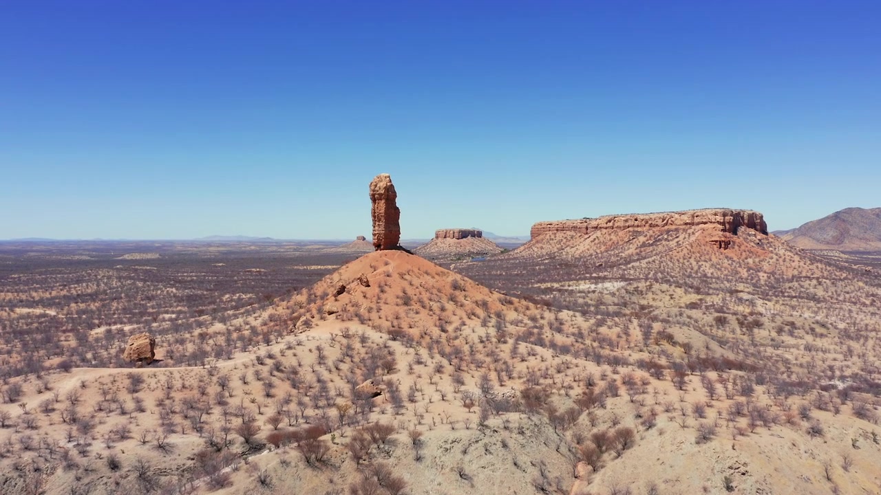 Rivelazione panoramica lenta con drone dell'ago di roccia Vingerklip, Namibia a mezzogiorno. Paesaggio arido e brullo, alberi spogli, cielo limpido e senza nuvole.