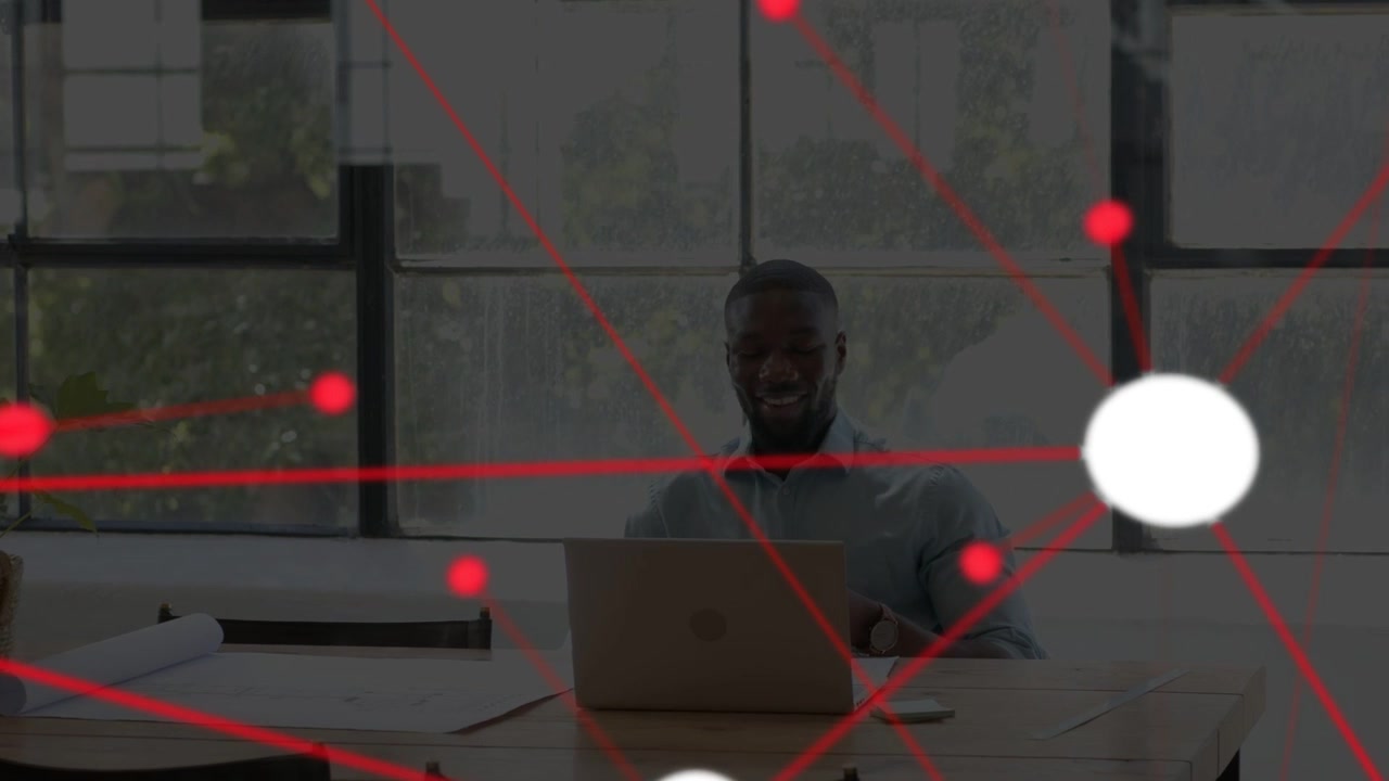 Man at desk tapping laptop, forming red network overlay with white node, smiling during review