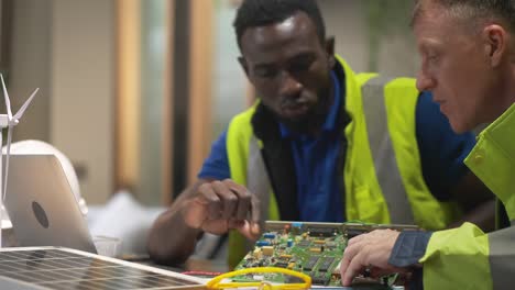 two american male engineers, sitting in a modern office, analyze work on renewable energy technology using solar energy and electric wind turbines. concept of technology and environment