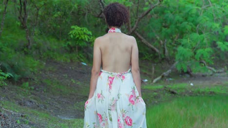 Una-Mujer-Joven-Caminando-En-La-Parte-Sombreada-De-Un-Parque-En-Un-Día-Soleado-Con-Un-Vestido-Largo-De-Flores