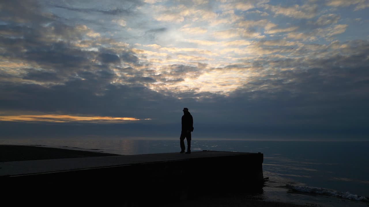movimiento lento de un hombre con silueta caminando desde el extremo de un muelle al atardecer en la playa de fleetwood, lancashire, reino unido