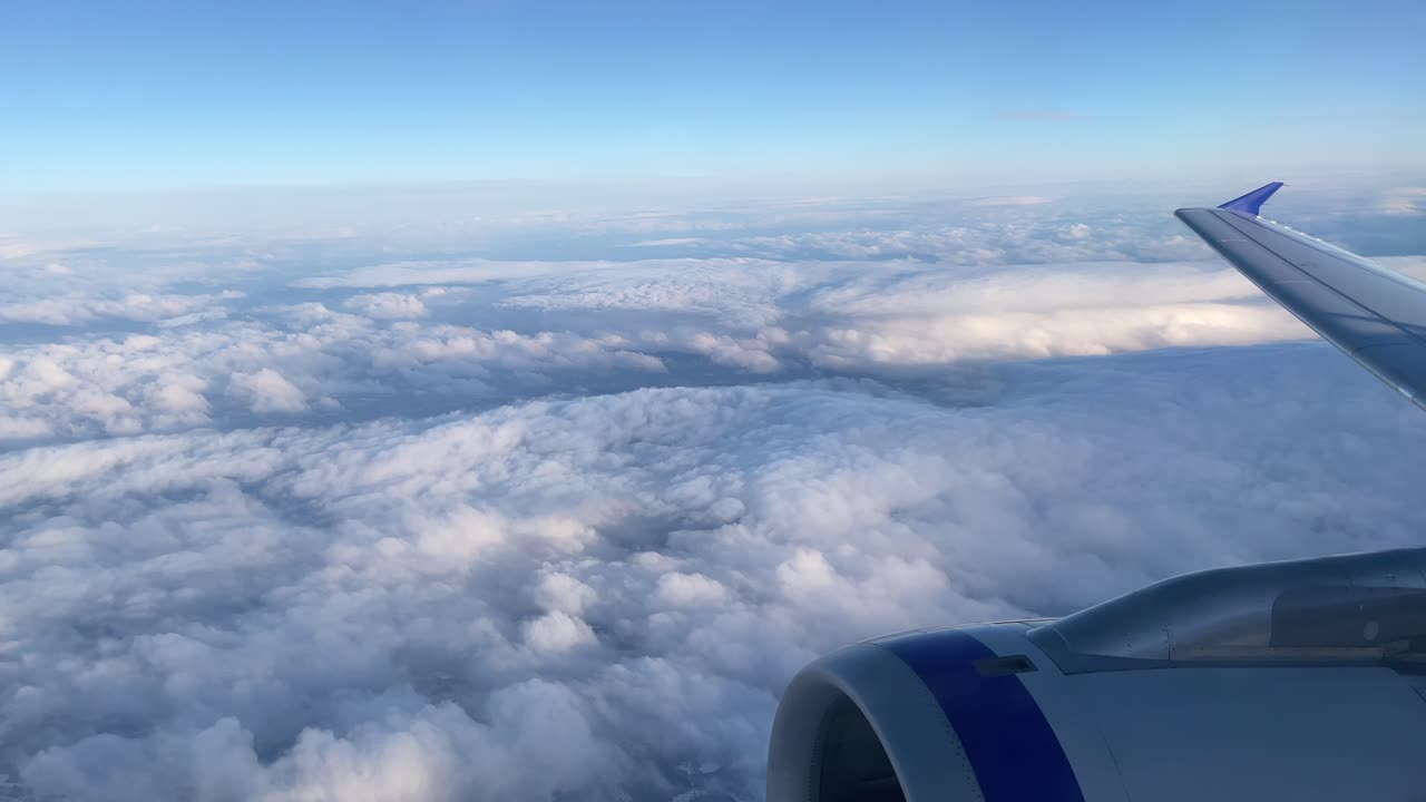 Udsigt fra et flyvindue højt over skyerne med blå himmel