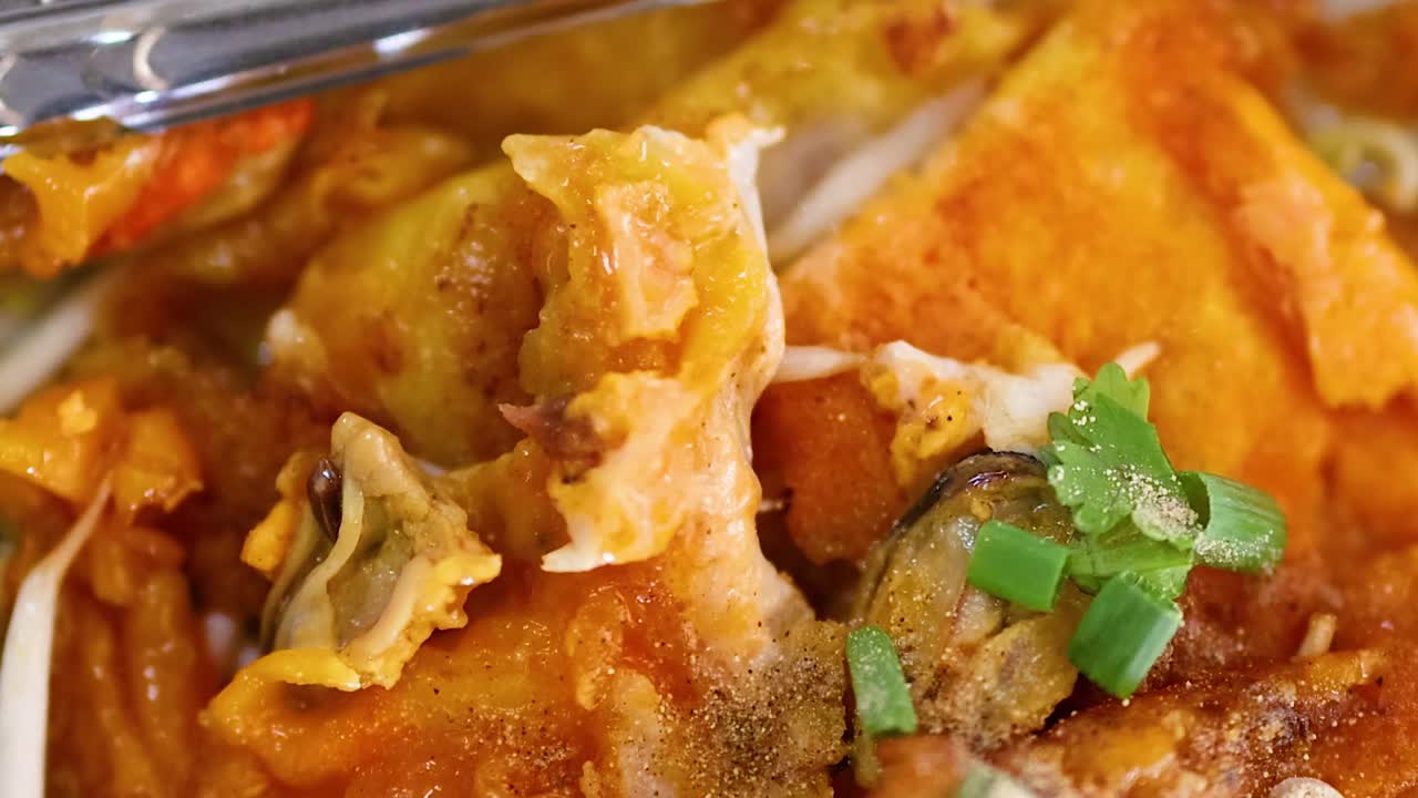 Detailed view of a crispy mussel pancake topped with fresh herbs and served with utensils.