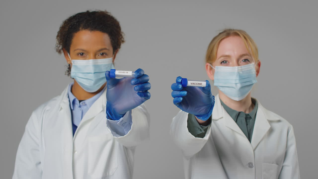 Studio Shot Of Lab Research Workers In Face Masks Holding Test Tubes Labelled Vaccine And Covid-19