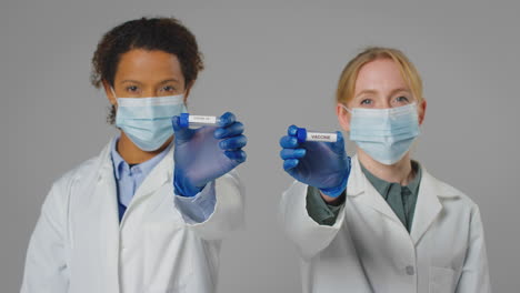 studio shot of lab research workers in face masks holding test tubes labelled vaccine and covid-19