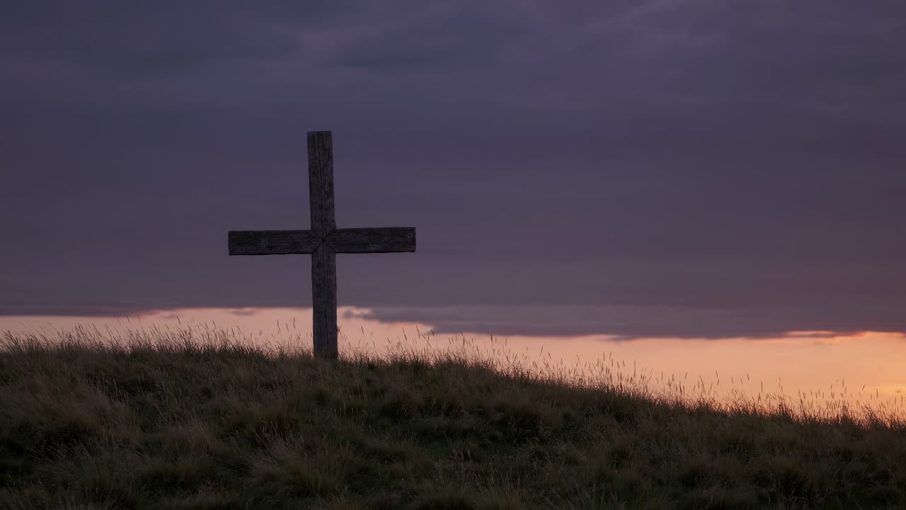 A wooden cross on a grassy hill at sunset, captured from a low angle